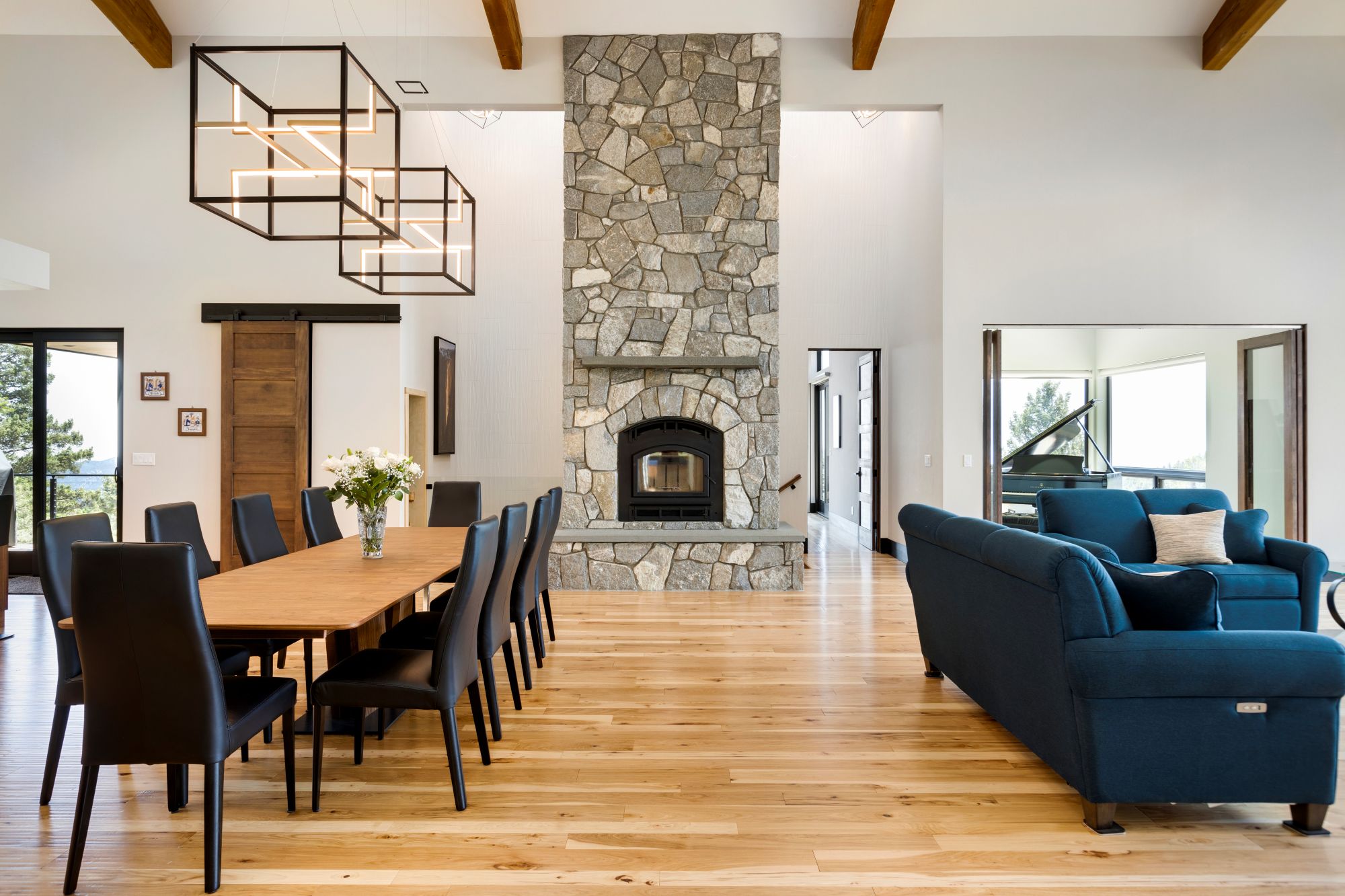 Great room with a two-story stone fireplace, exposed beams, a long wood dining table, and wide-plank floors