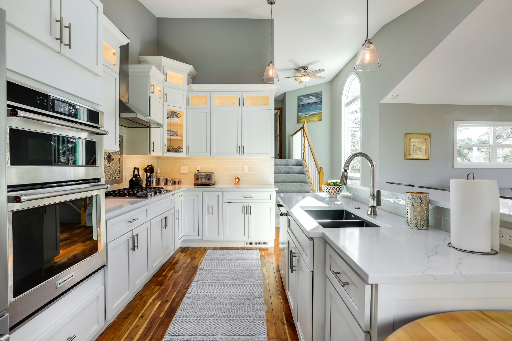 White kitchen with a quartz island, wall ovens, and hardwood floors