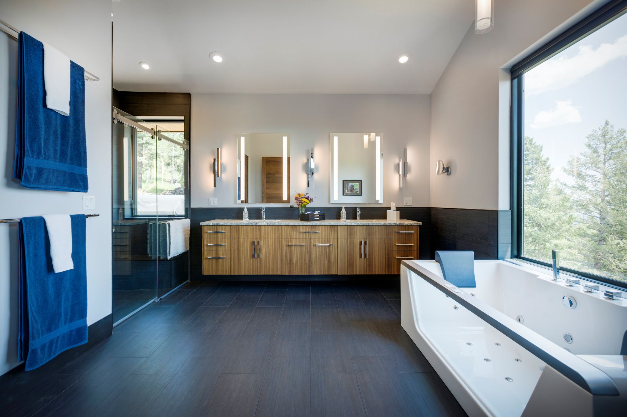 Primary bathroom with a floating wood double vanity, soaking tub, and a picture window looking into the pines