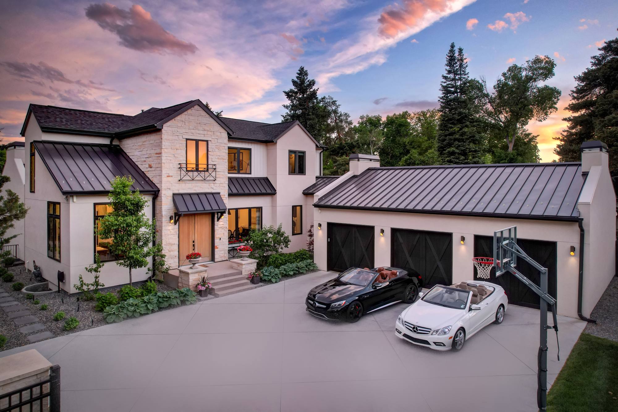 Two-story stone and stucco home photographed at twilight with warm window light and a lit driveway